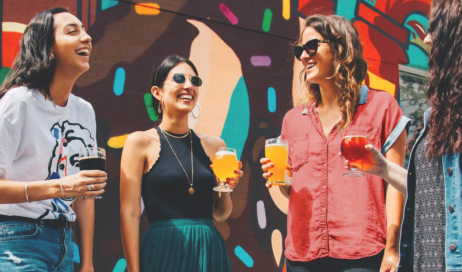 lifestyle image of people standing with drinks in-hand in front of a large colorful mural